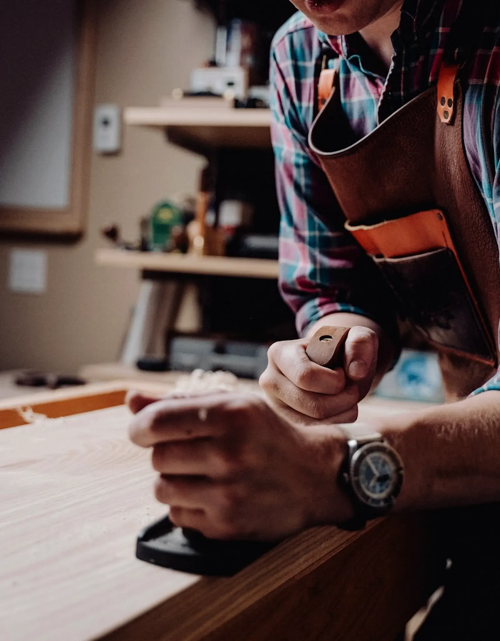 Artisan menuisier au rabot, penché sur une planche de bois dans son atelier.