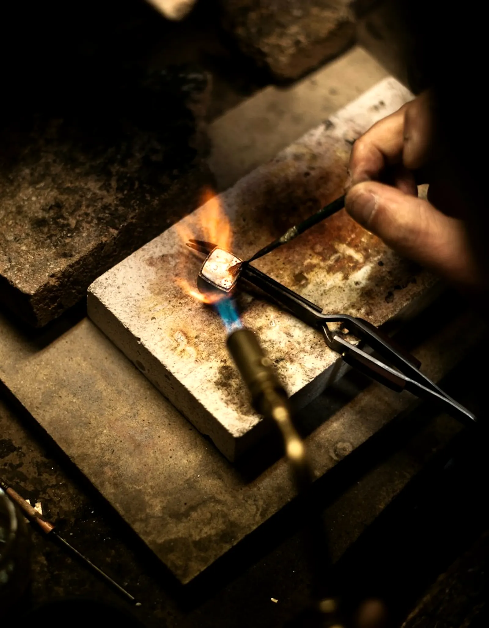 Artisane brasant une pièce de bijouterie fine à l'établi, geste précis à la loupe.
