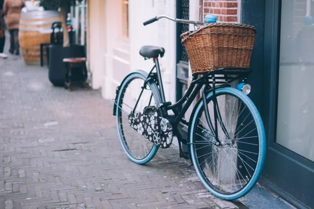 Vélo à panier en osier garé contre une façade, dans une rue pavée