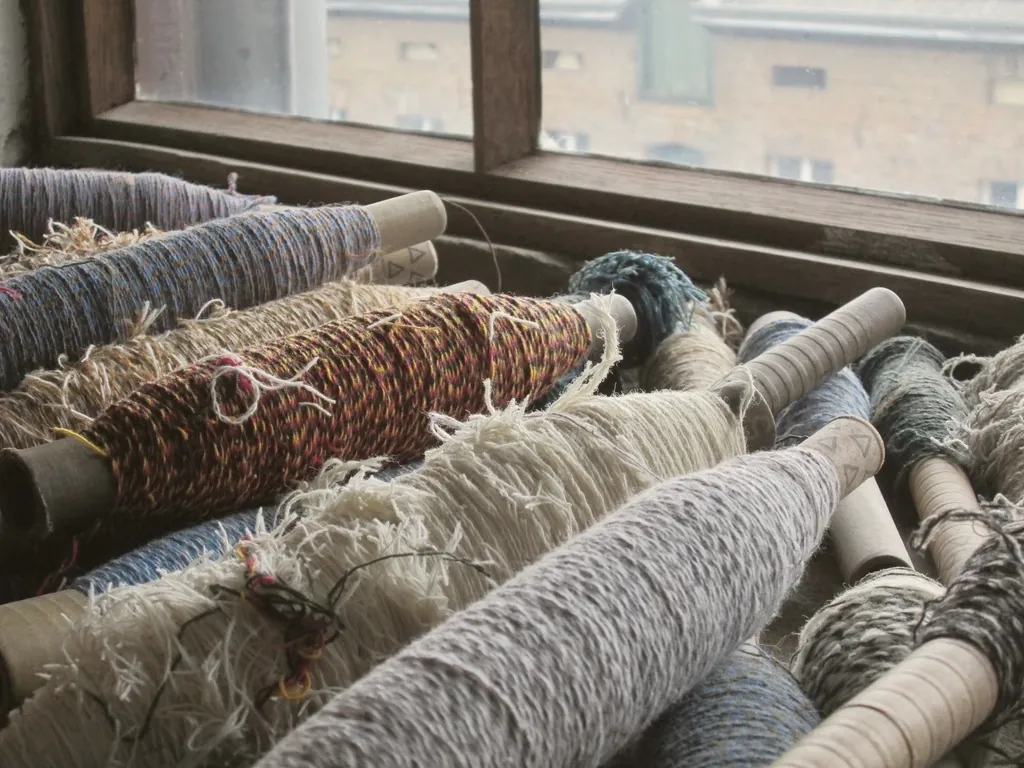 Des bobines de fil de laine écru, gris et brun posées près d'une fenêtre d'atelier