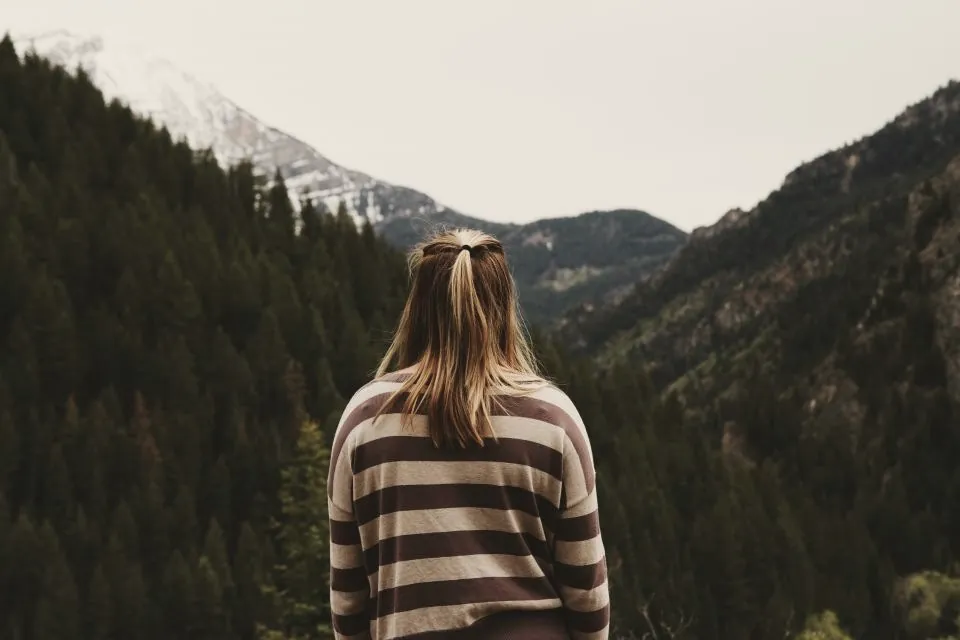De dos, face à une vallée de montagne, une femme porte le pull rayé Le Marin