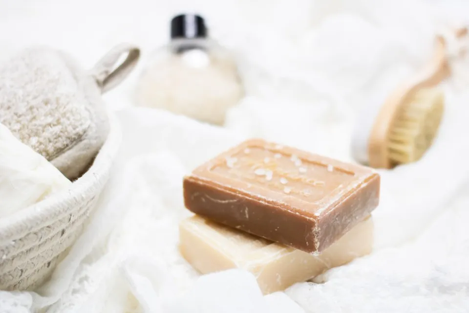 Une barre de savon terre cuite posée sur une barre crème, sur du lin, près d'une brosse en bois