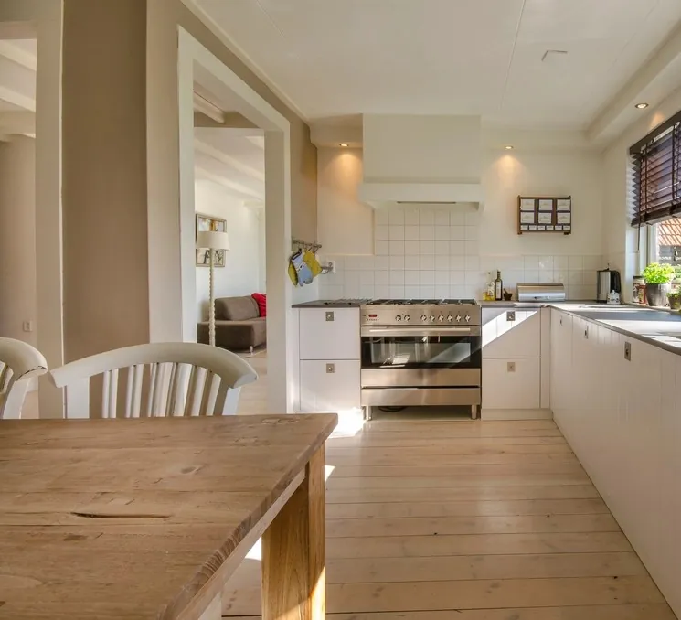 Grande cuisine en U, façades peintes blanc cassé, parquet clair et table en chêne au premier plan