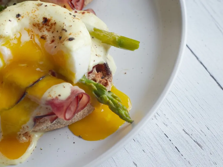 Œufs pochés sur pain grillé, sauce hollandaise et asperges vertes, le jaune coule sur l'assiette blanche
