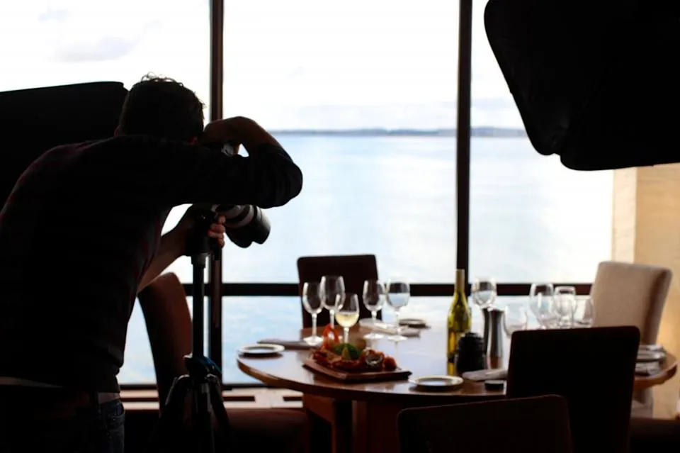 Silhouette d'une photographe à contre-jour dans une salle de restaurant, face à une table dressée