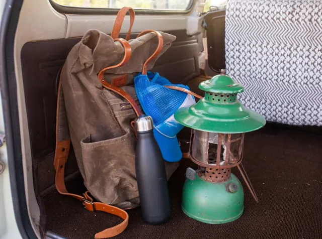 Le sac en toile cirée posé dans le coffre d'un van, à côté d'une gourde et d'une lanterne